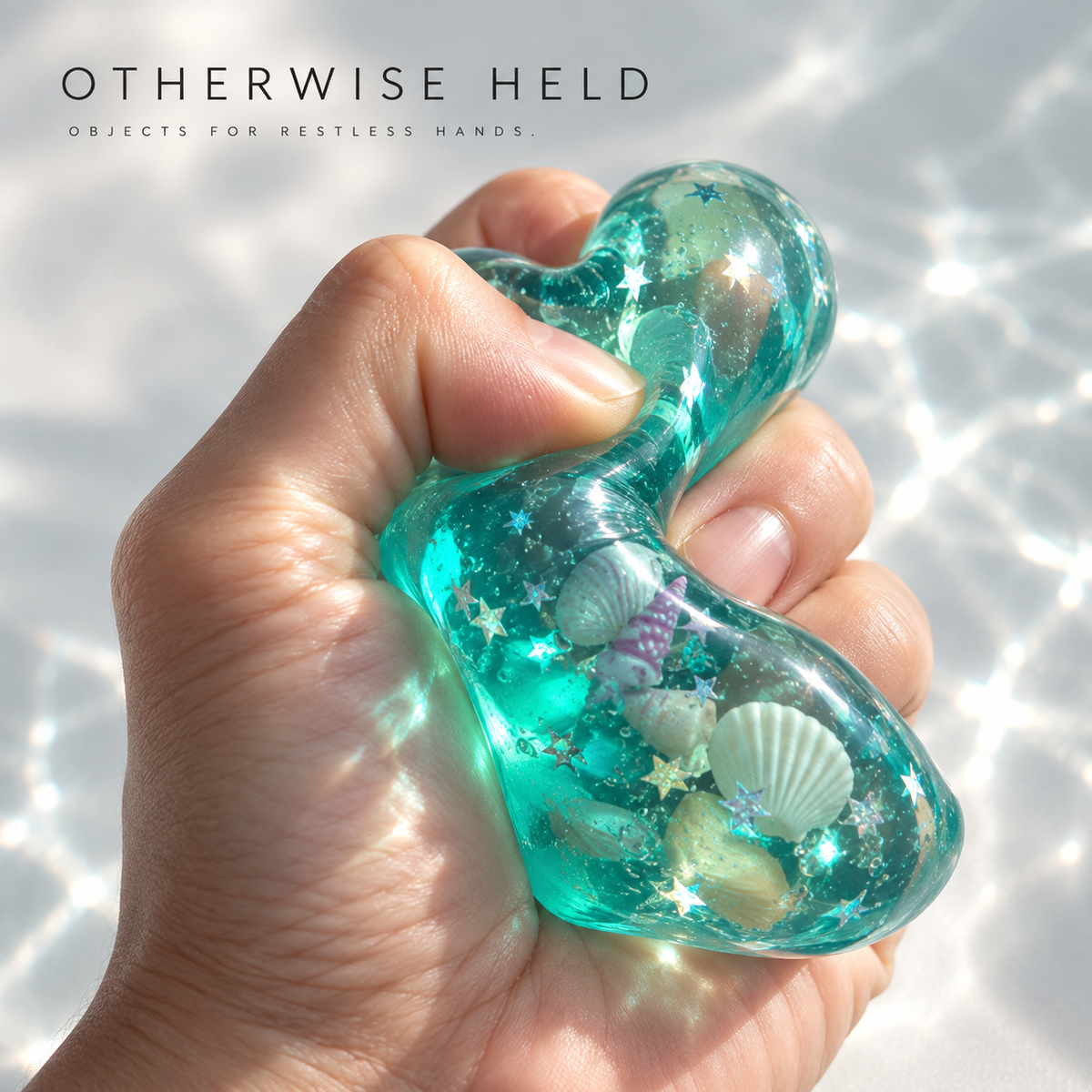 OH 05 Ocean, hand squeezing the translucent teal cube as the shells and stars shift inside